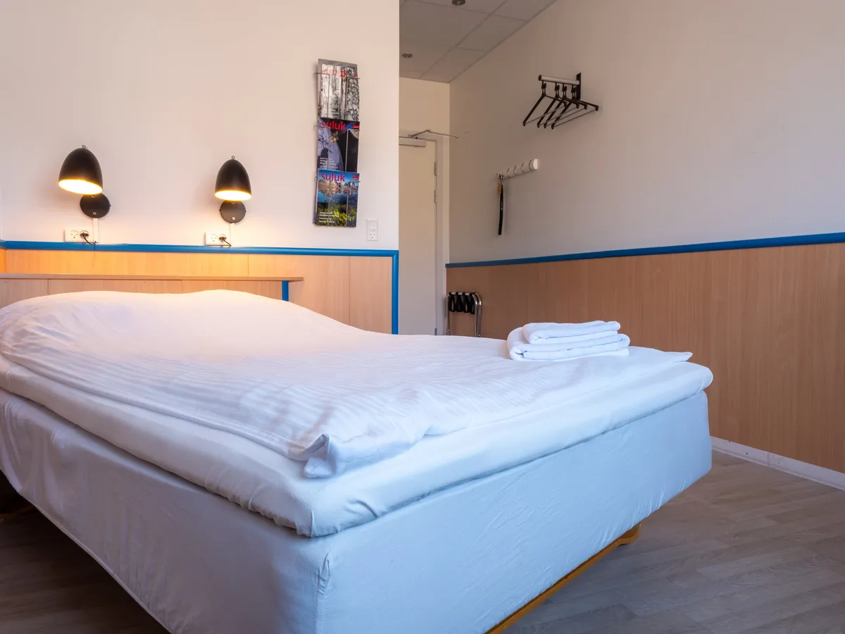 The full bed in a single room, made up with white linen and towels, with two reading lamps above it.